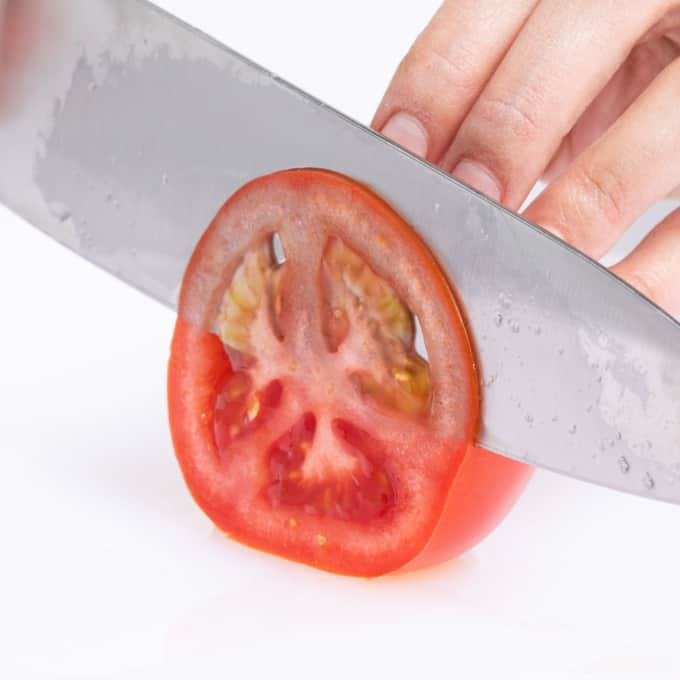 A large knife slices through a tomato.